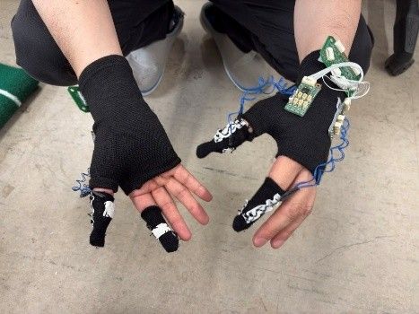 指先にセンサを取り付けた黒いグローブを両手にはめ、手のひらを上に向けている様子