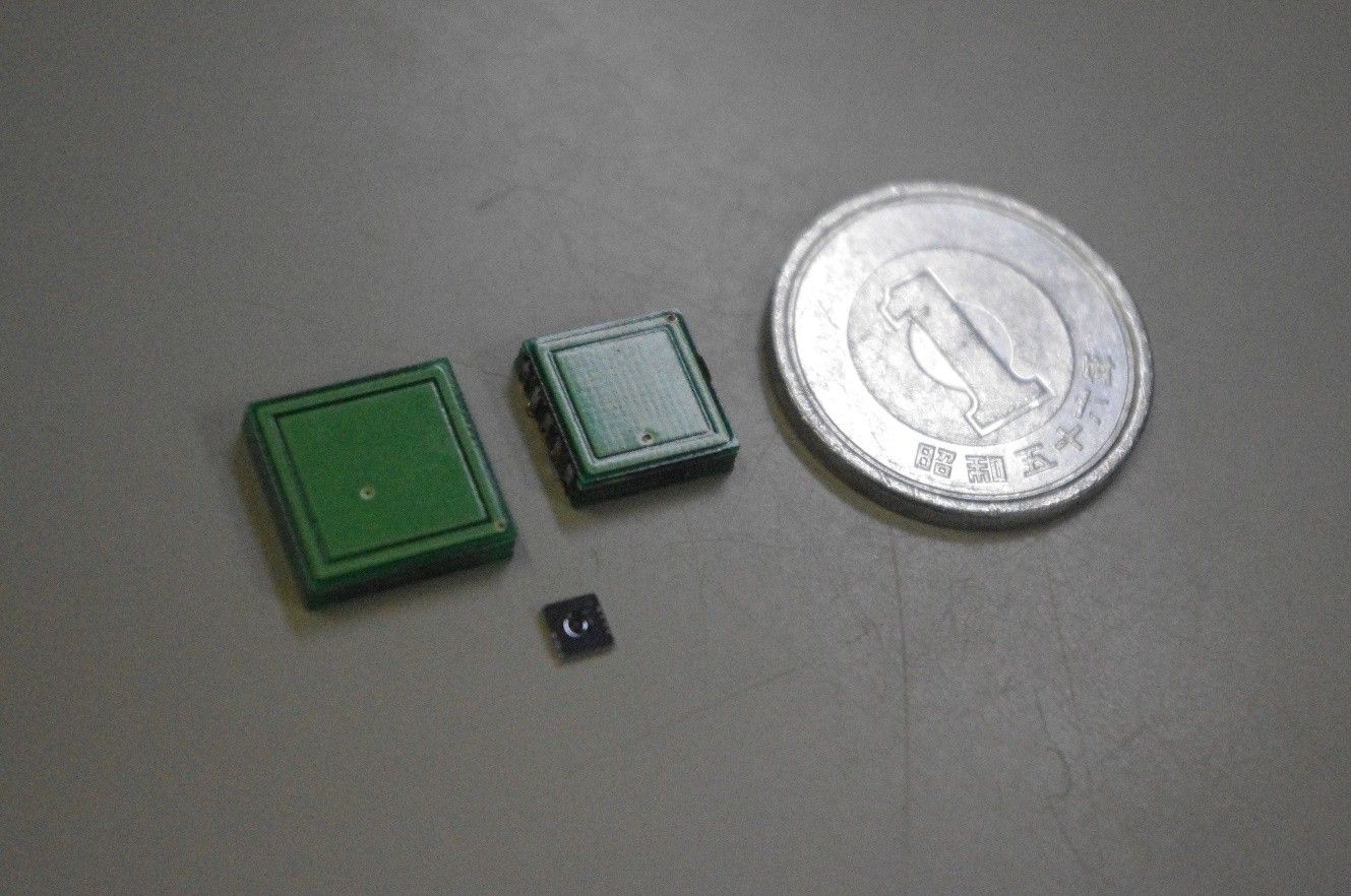 緑色の四角い触覚センサ2個と小さな黒いチップを、大きさの比較のための1円硬貨と並べた写真